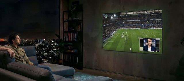 Un hombre mira un partido de fútbol en un televisor Samsung de gran formato desde el sofá