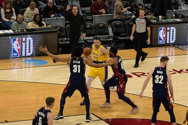 Luka Dončić, con el uniforme amarillo de los Lakers, conduce el balón ante Jarrett Allen y Donovan Mitchell, de los Cavaliers