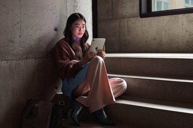 Una joven lee en un iPad mini color blanco estelar sentada en una escalera de concreto