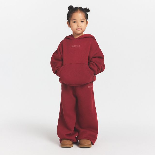 Niña con sudadera con capucha y pantalón de felpa rojo ladrillo de la colección infantil de Skims