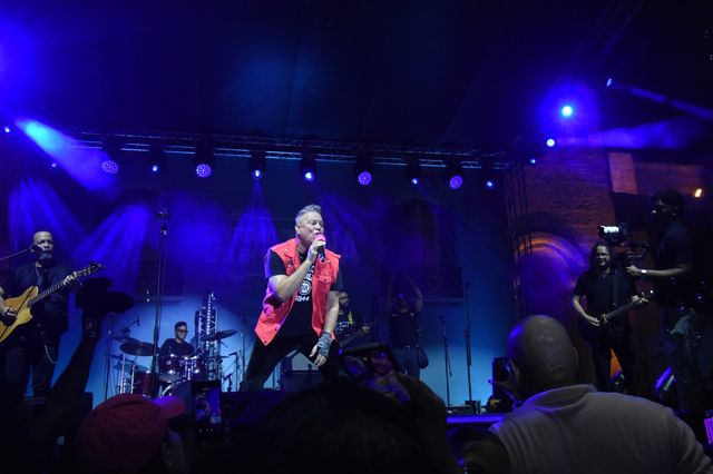 El cantante de Aljadaqui, con chaleco rojo, canta junto a su banda bajo luces azules