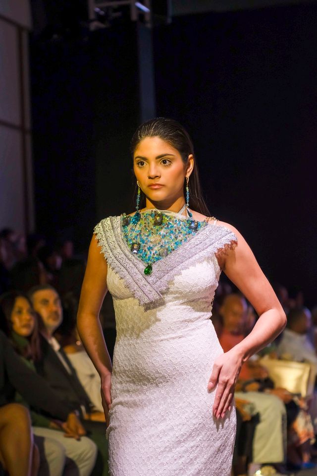 Modelo con un collar de pedrería sobre un vestido blanco en la pasarela