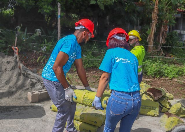 Dos voluntarios con cascos rojos cargan sacos de cemento