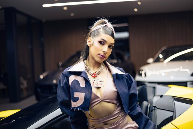 La Gigi con chaqueta de mezclilla junto a un auto deportivo amarillo