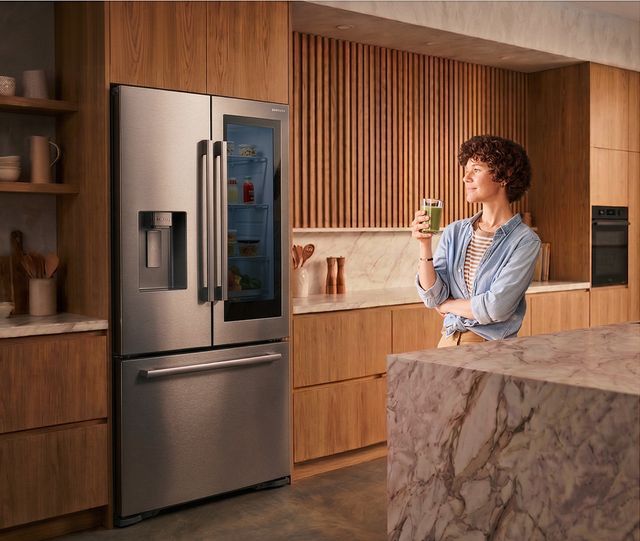 Un hombre bebe junto a una refrigeradora Bespoke AI AutoView en una cocina