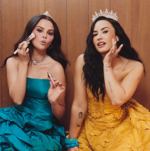 Selena Gomez, con vestido turquesa, y Demi Lovato, con vestido dorado y corona, en la campaña Still Making Each Other Blush de Rare Beauty