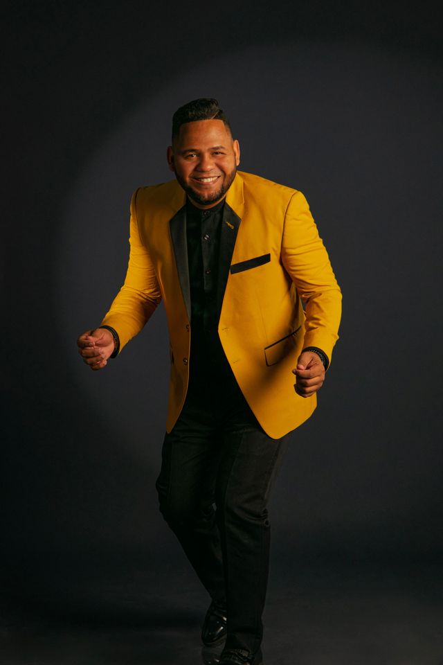 Wilbert Taveras, con chaqueta amarilla, baila frente a un fondo oscuro