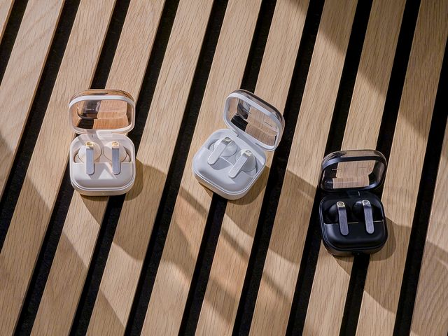 Galaxy Buds4 en sus estuches abiertos, en blanco y negro, sobre una superficie de listones de madera