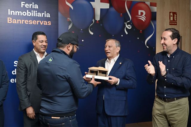 Entrega del galardón con forma de casa a Wester Hernández frente al panel de la Feria Inmobiliaria Banreservas