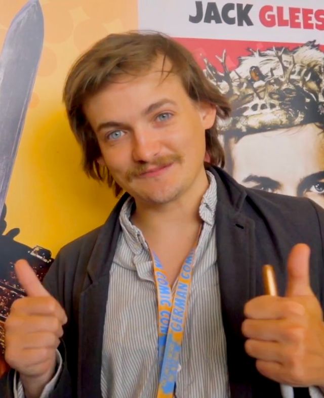Jack Gleeson levanta los pulgares frente a un cartel con su nombre en la German Comic Con de 2022