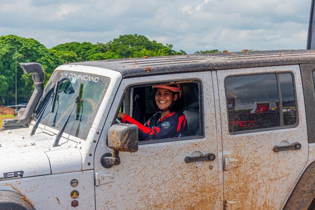 Una piloto sonríe desde un Jeep blanco cubierto de lodo durante la competencia