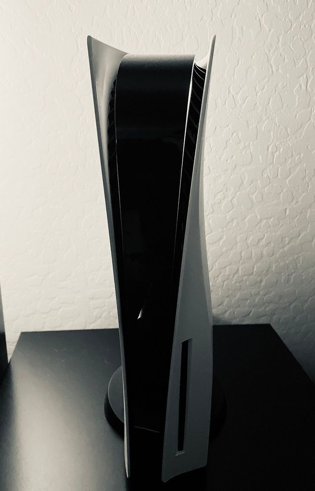 Una consola PlayStation 5 blanca, de pie sobre una mesa negra frente a una pared clara
