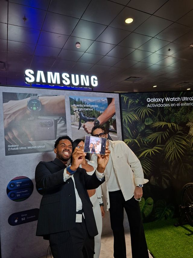 Tres invitados posan con los nuevos relojes Galaxy Watch en el stand de Samsung