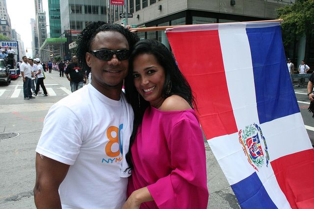 Celinés Toribio, vestida de fucsia, sonríe junto a una bandera dominicana en el Desfile Dominicano de Nueva York