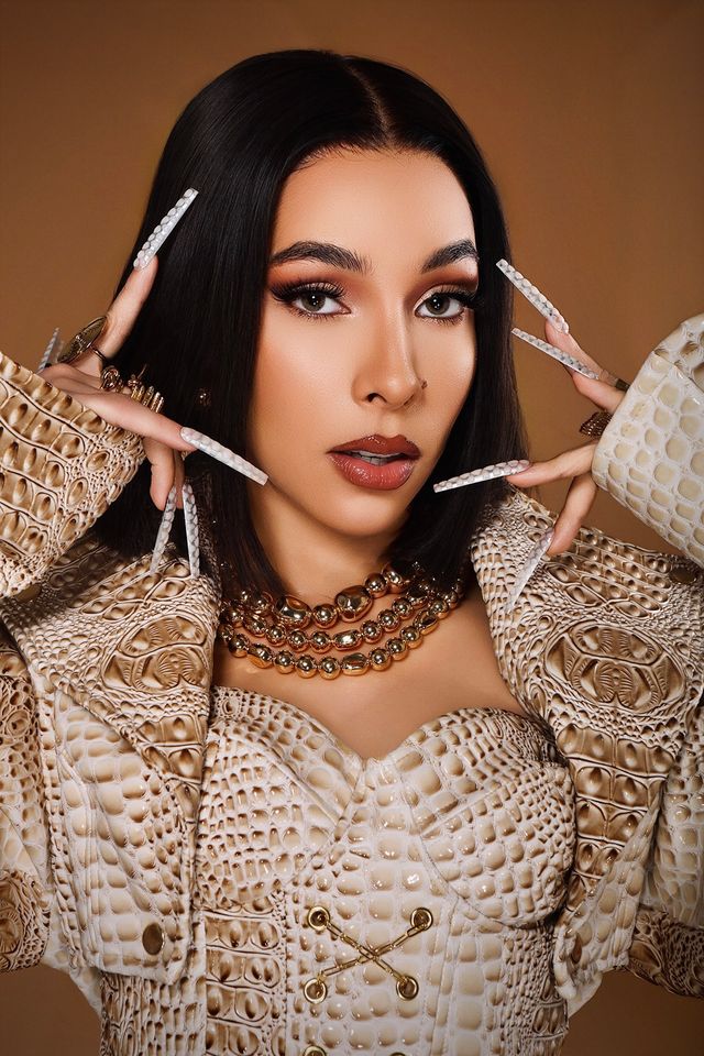 La Gigi con conjunto de textura trenzada y uñas largas sobre fondo marrón