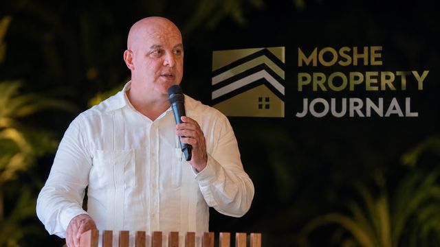Moshe Gil habla con un micrófono frente al logo de Moshe Property Journal
