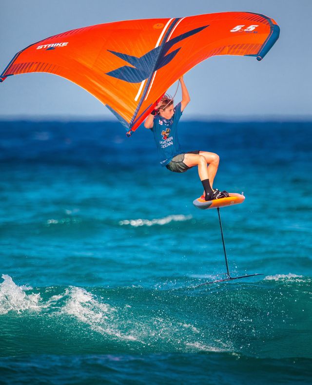 Un atleta de wingfoil se eleva sobre el agua con su ala naranja