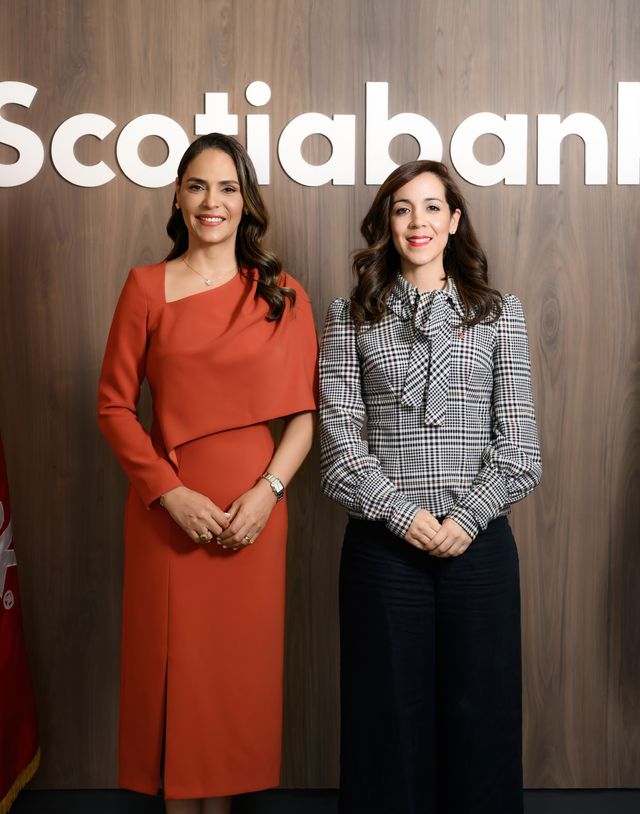 Sadery Abreu, de vestido naranja, junto a Rosalía Muñoz frente al logo de Scotiabank