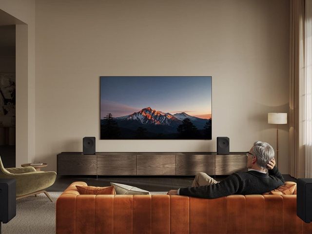 Dos bocinas Samsung Music Studio 7 a los lados de un televisor en una sala con sofá naranja