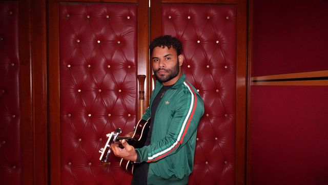 Joe Blandino toca la guitarra frente a una pared roja acolchada