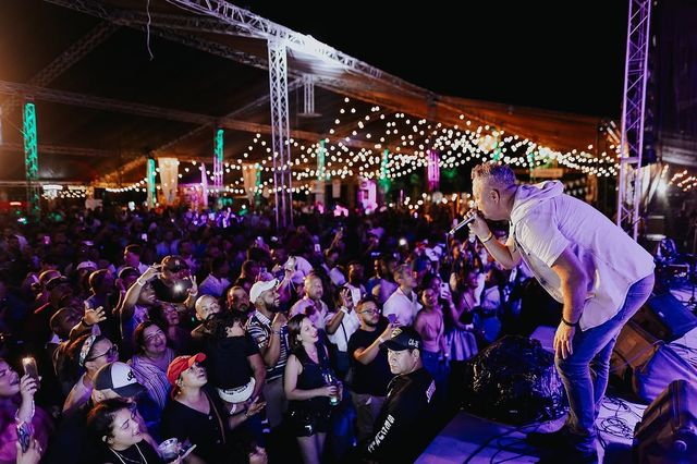 Aljadaqui en concierto: el cantante se inclina hacia el público bajo una carpa decorada con bombillos