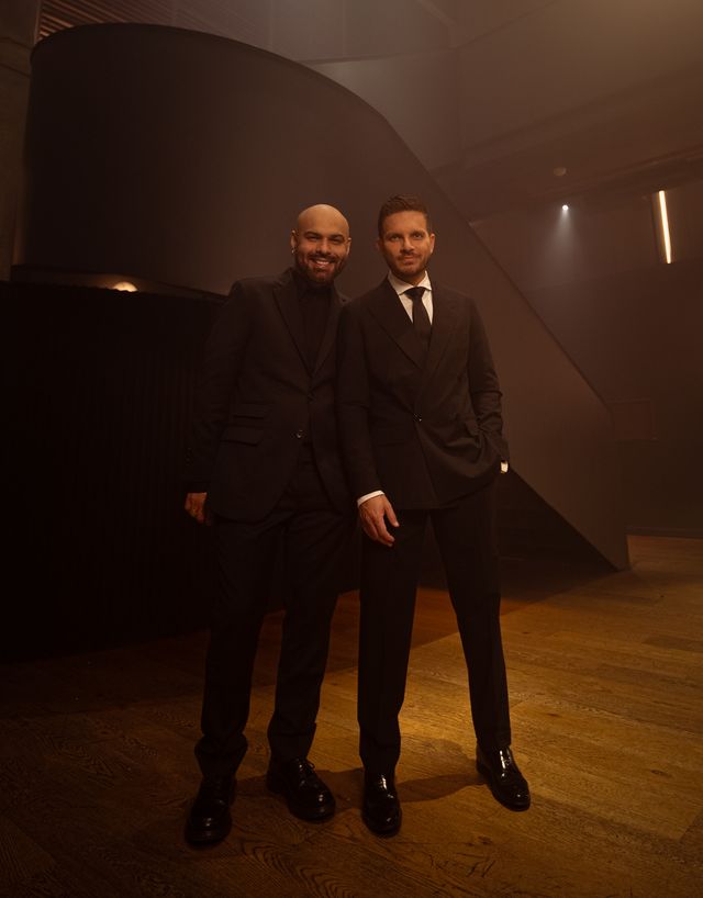 Omar Enrique y Omar Acedo, de traje oscuro, de pie en un estudio