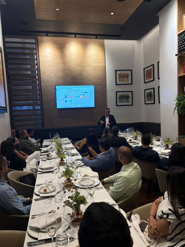 Asistentes siguen la presentación de Business IT en mesas decoradas con centros de flores