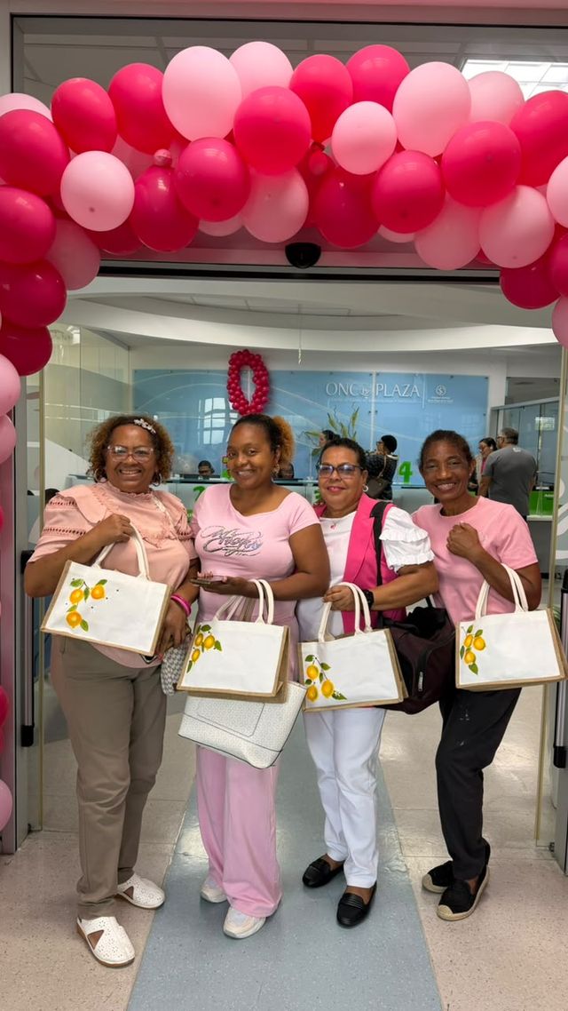 Pacientes de Onco Plaza muestran los bolsos que decoraron en el taller de RADONIC, bajo un arco de globos rosados