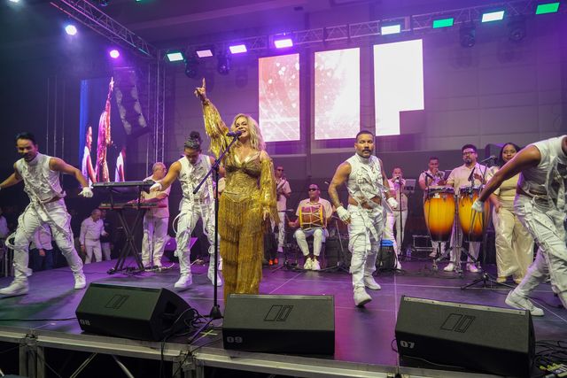 Miriam Cruz levanta el brazo frente a su orquesta y bailarines