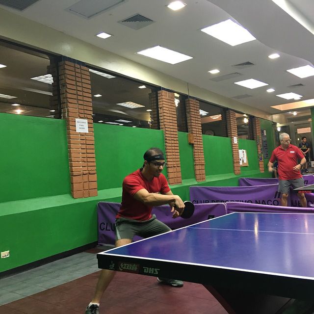 Un jugador con camiseta roja devuelve la pelota en una mesa de tenis de mesa azul en un club de Santo Domingo