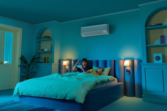 Una pareja descansa en un dormitorio iluminado en azul con un aire acondicionado WindFree