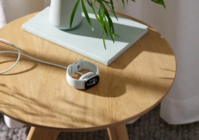 La pulsera Google Fitbit Edge con correa blanca se carga sobre una mesita de madera