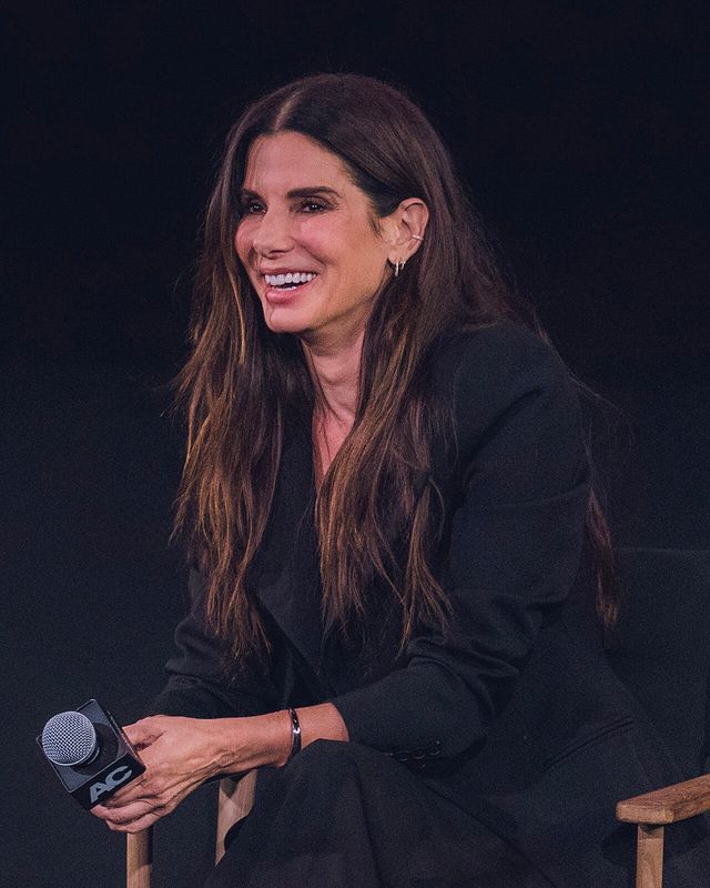 Sandra Bullock sonríe sentada en un escenario, con micrófono en la mano, en el Teatro Egipcio de Los Ángeles en octubre de 2024