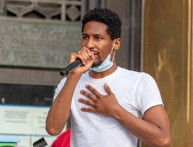 Jon Batiste habla con un micrófono y la mano en el pecho durante un acto de Juneteenth en Brooklyn en 2020