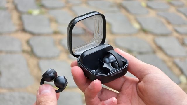 Una mano sostiene el estuche abierto de los Galaxy Buds On y la otra uno de los audífonos de clip