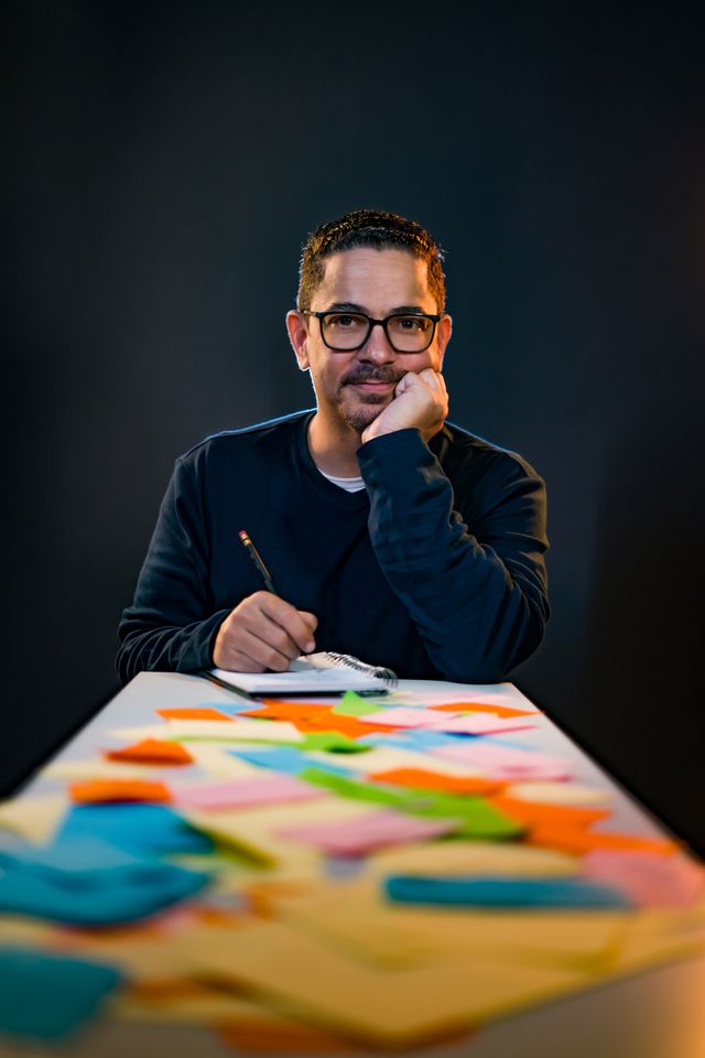 Luis José Germán sentado ante una mesa cubierta de notas de colores