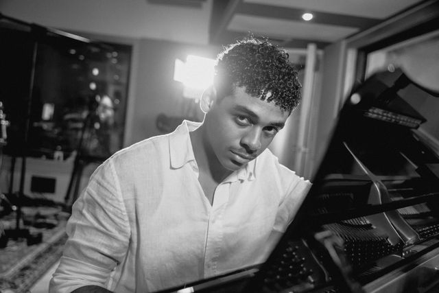 Ansel Mauricio, en blanco y negro, sentado al piano de cola en un estudio de grabación