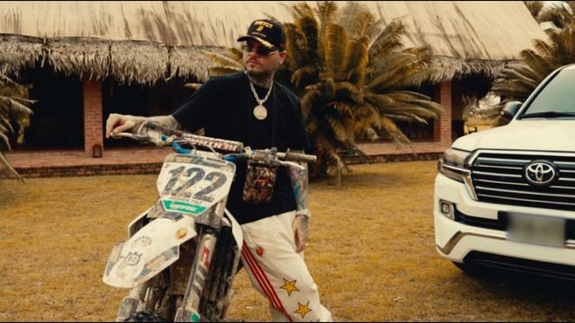 Farruko, con gorra negra y gafas oscuras, apoyado en una moto de motocross en su video «Formal»