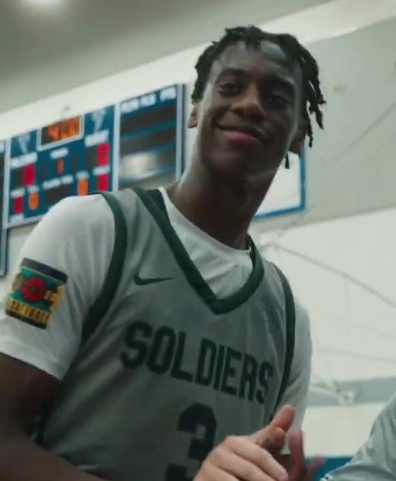 AJ Dybantsa sonríe con la camiseta gris de Soldiers en un gimnasio en 2024