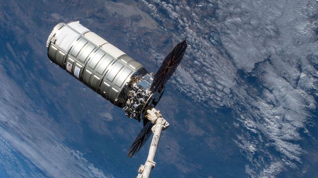 La nave de carga Cygnus XL sujeta por el brazo robótico Canadarm2 de la Estación Espacial Internacional, con la Tierra de fondo