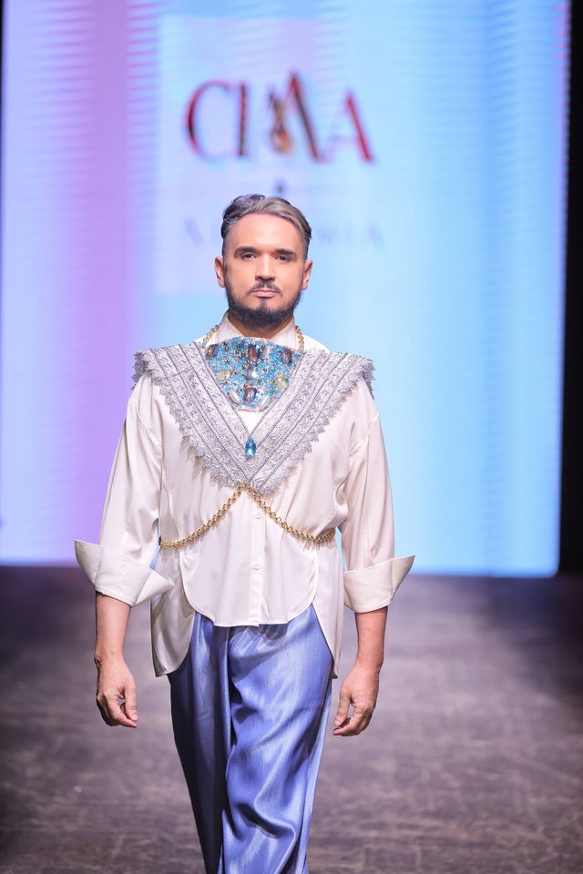 Un modelo con camisa blanca y una pieza masculina de CIMA sobre el pecho