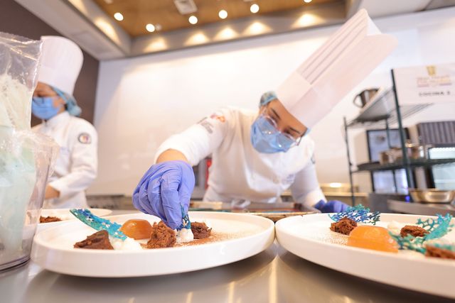 Un cocinero con guantes emplata postres
