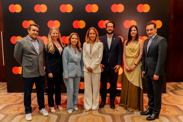Ejecutivos y conferencistas de Mastercard Day posan frente a un fondo con el logo de Mastercard