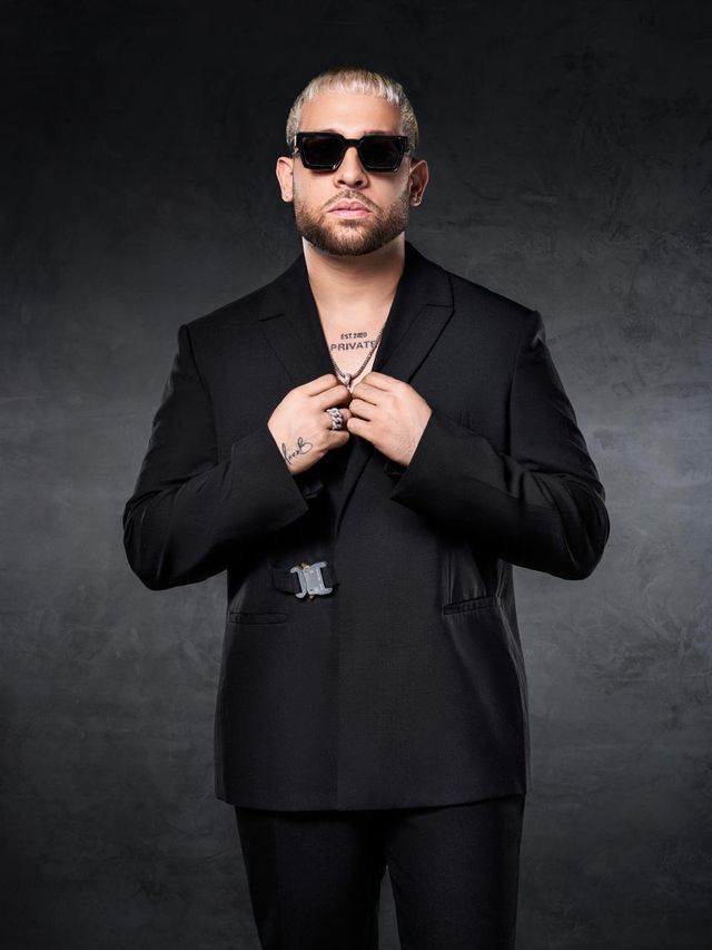 Mark B con traje negro y gafas oscuras ajustándose la chaqueta