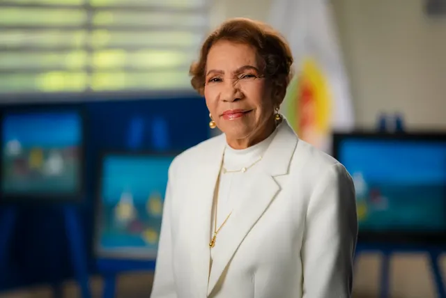 Ada Alba Drullard, de chaqueta blanca, en un salón con pinturas al fondo