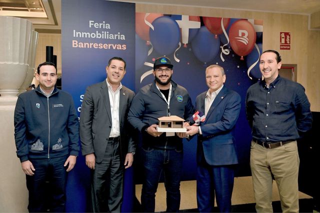 Wester Hernández sostiene el galardón con forma de casa junto a cuatro ejecutivos en la Feria Inmobiliaria Banreservas
