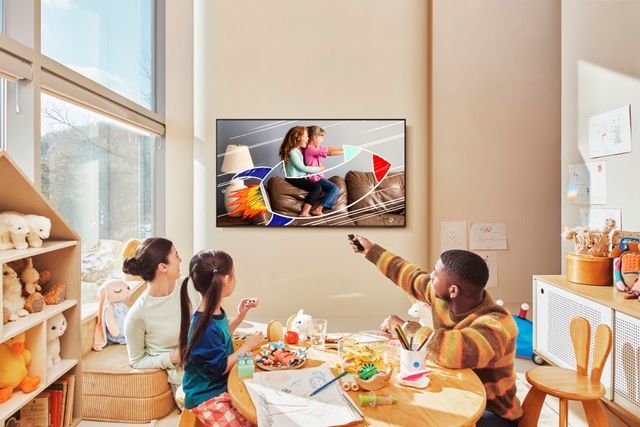 Familia con niños frente a un televisor Samsung colgado en la pared de una sala luminosa