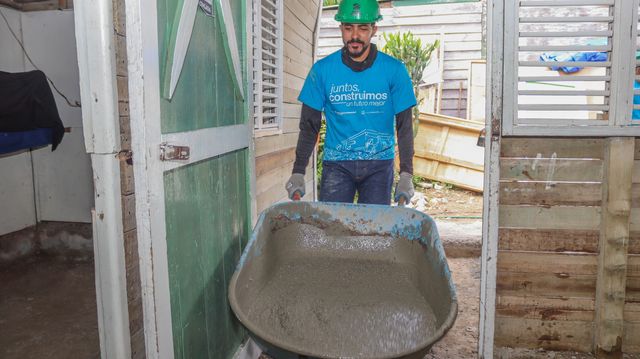 Un voluntario lleva una carretilla con concreto hacia el interior de una vivienda