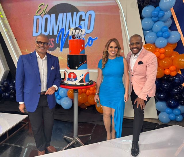 Conductores de «El Domingo es Mío» en el set junto a un pastel y globos azules y naranjas