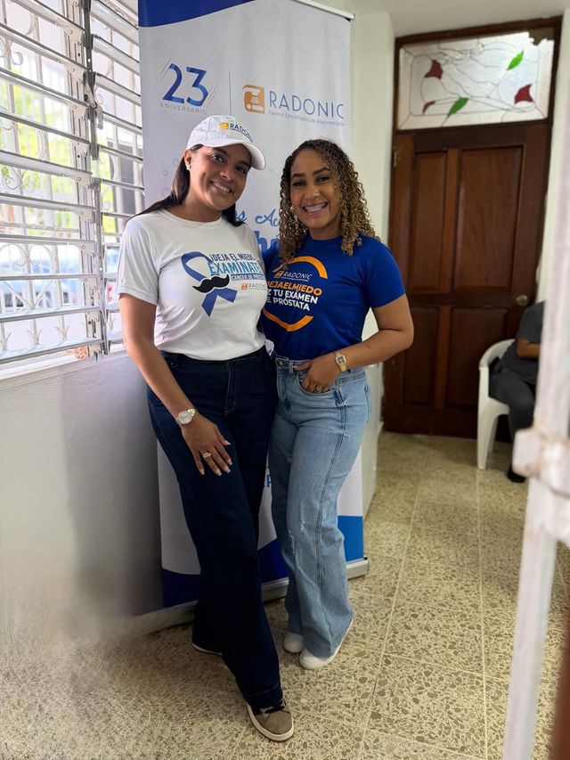 Dos voluntarias con camisetas de la jornada junto a un banner de RADONIC